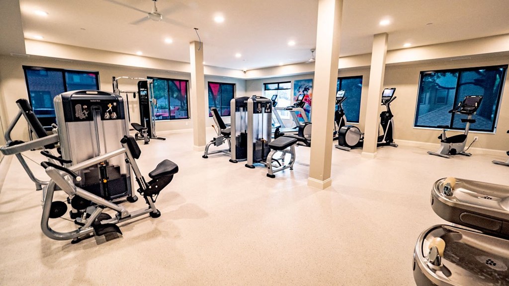 Modern gym here at Daymark Uptown Apartment Homes with various exercise machines, including bikes and weight equipment, large windows, bright lighting, and a clean, spacious feel.