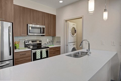 Modern kitchen here at Escape Apartments with wooden cabinets, stainless steel appliances, and a washer-dryer in an alcove. Bright and clean ambiance with a white countertop.