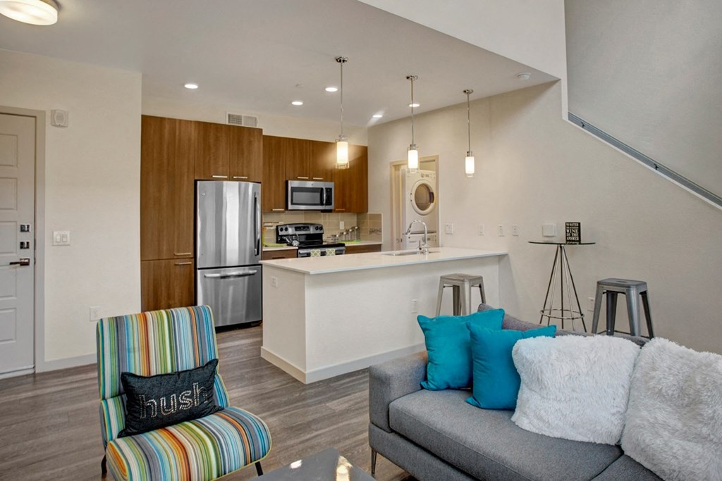 a living room with a couch and a chair in front of a kitchen with a stove and