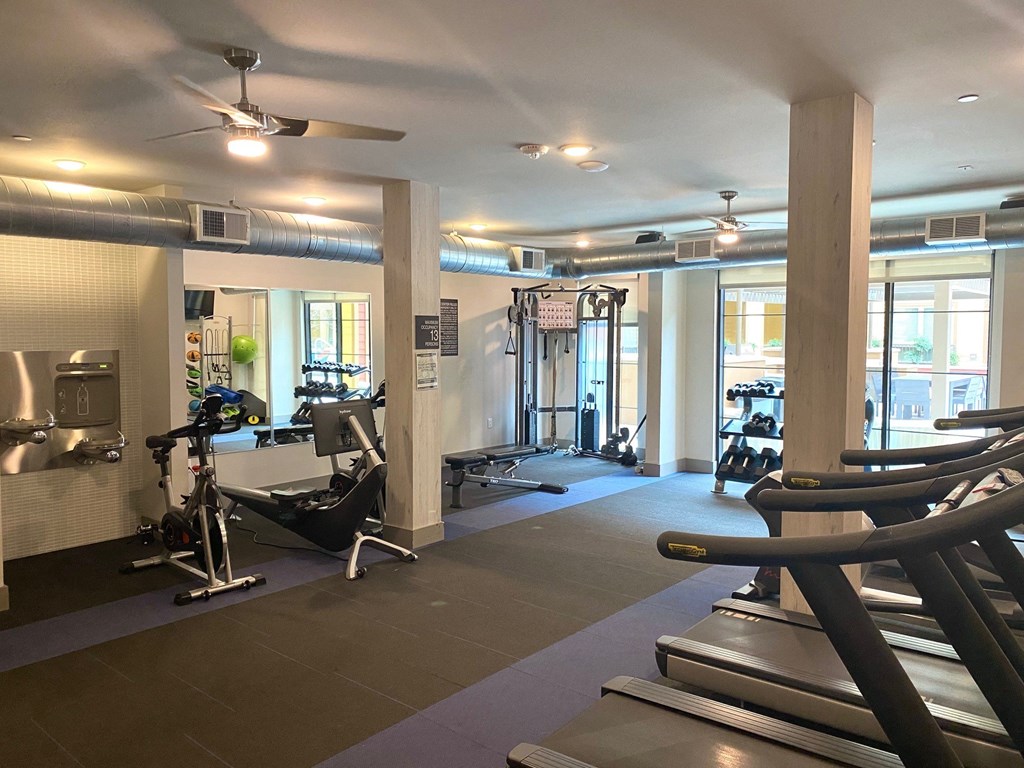 Modern gym here at Florence at the Harbor Apartment Homes with treadmills, exercise bike, and weightlifting area. Bright, spacious, with large windows and a sleek, organized layout. Calm atmosphere.