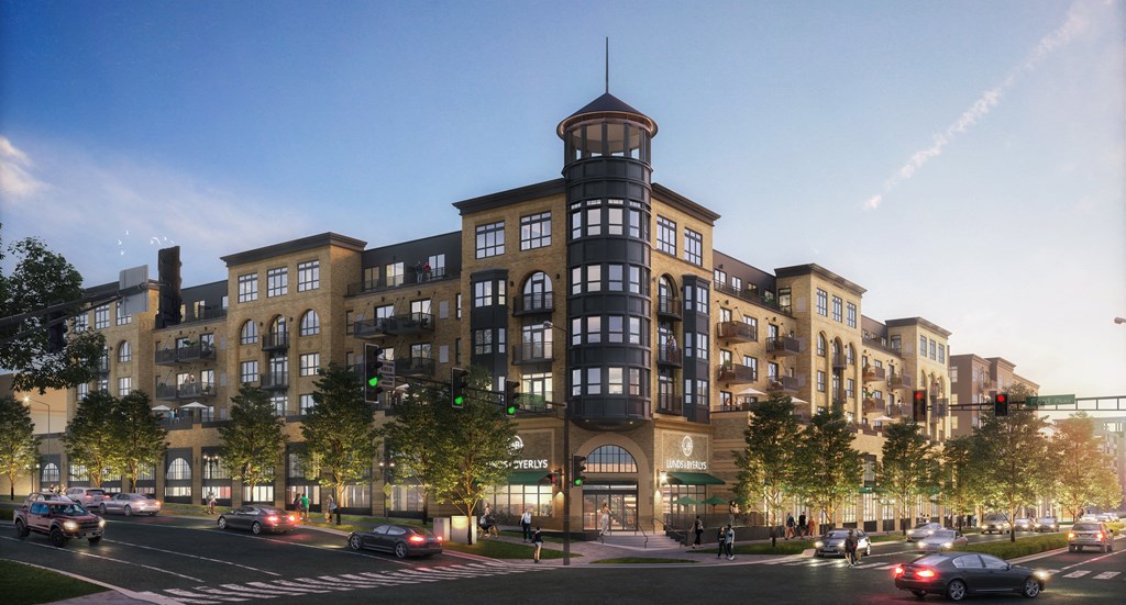 Street view of our modern The Collection at Highland Bridge Apartment Homes building at dusk with warm lighting, numerous windows and balconies, surrounded by trees and cars, creating a lively urban atmosphere.