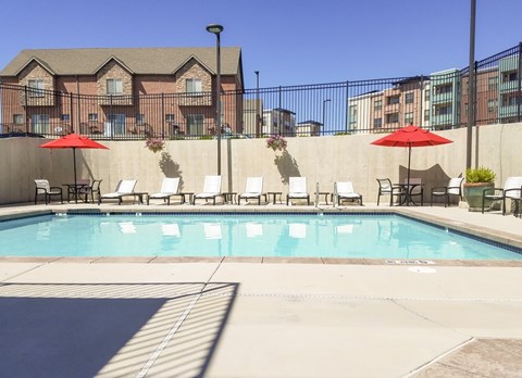 A pool with red umbrellas and chairs in front of a building.