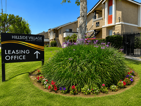 A leasing office sign for Hillside Village Apartments is in front of a landscaped area.