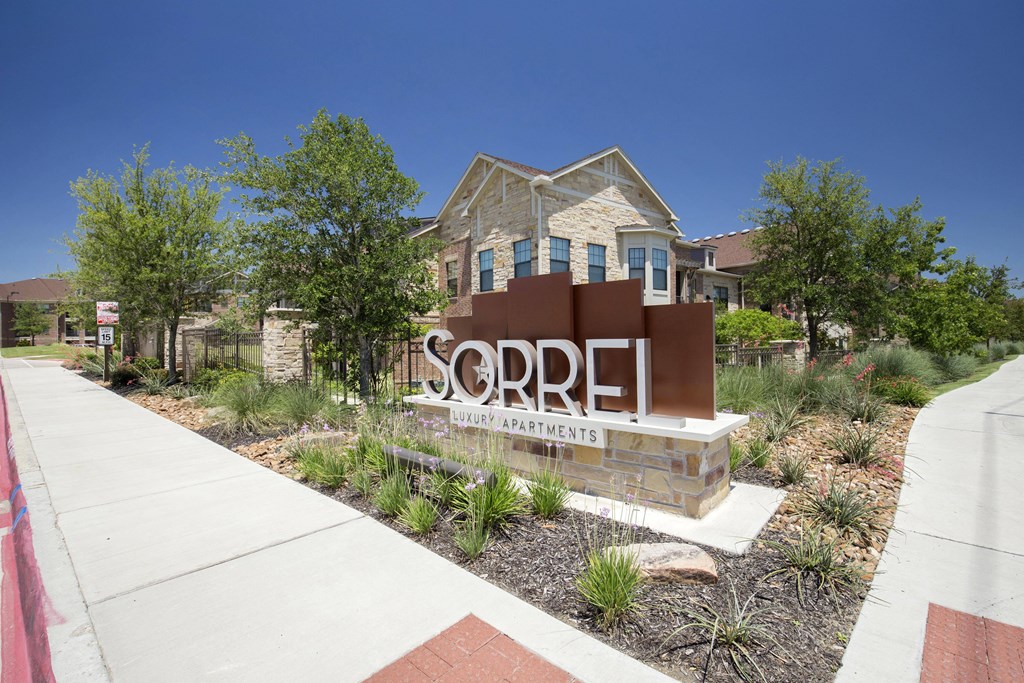 Sign for Sorrel Luxury Apartments with modern design and landscaped greenery, set against a sunny sky and building facade, conveying elegance.