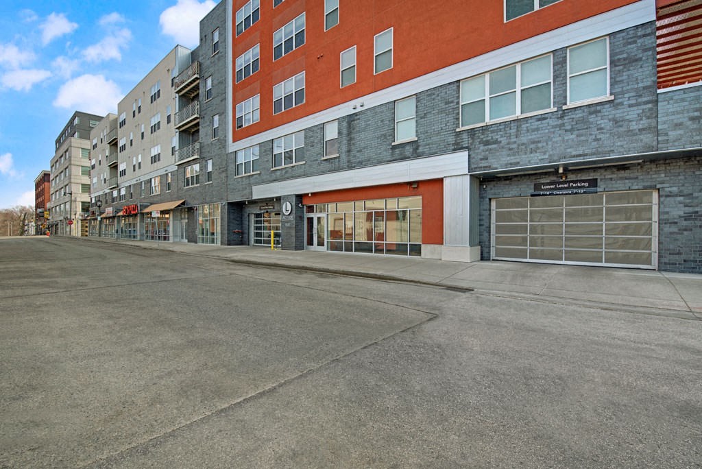 Street scene showing modern Latitude Apartment buildings with red and gray facades, large windows, and a parking garage.