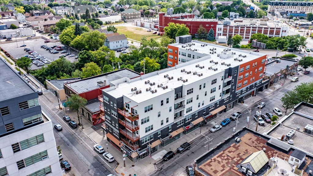 Aerial view of a Latitude Apartments featuring modern apartment buildings with white and orange facades. Surrounding greenery and parking lots can be seen, contributing to a tranquil urban atmosphere.