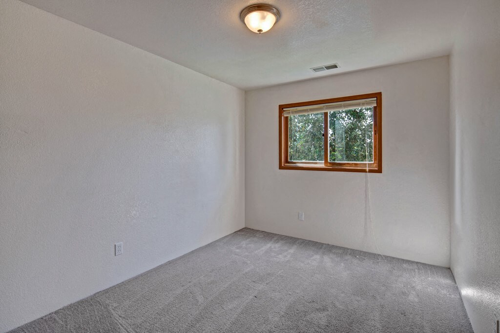 Empty bedroom here at Legacy West Apartments with light gray carpet and white walls. A single window with wooden trim lets in natural light, creating a calm and simple ambiance.
