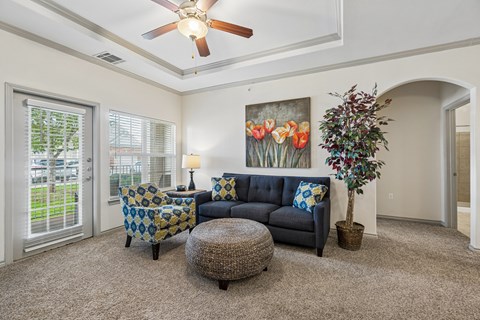 A living room with a blue couch, a chair, a table, and a ceiling fan.