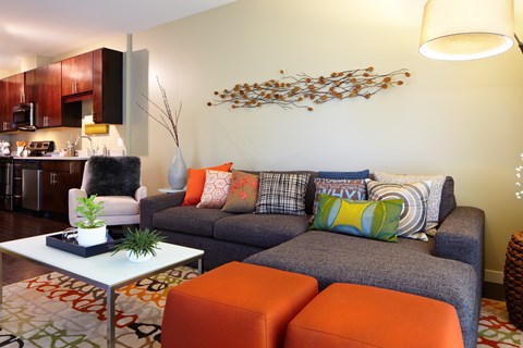 A living room with a grey couch and orange ottoman.