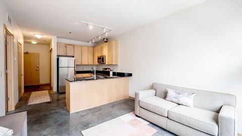 A modern living room with a grey couch and a kitchen area in the background.