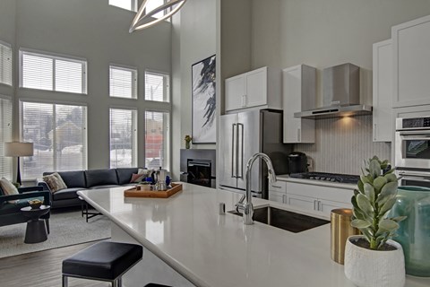 A modern kitchen with a long white island and stainless steel appliances.