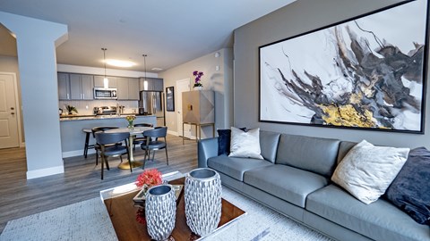 A modern living room with a grey couch and a large abstract painting on the wall.