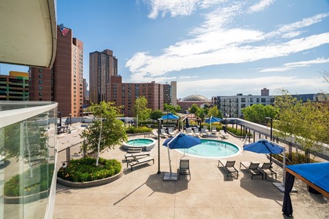 A vibrant rooftop pool here at LPM Apartments showcasing a spacious sun deck with a sparkling swimming pool, surrounding lounge chairs, and shaded cabanas, set among landscaped greenery and offering elevated city views that create an inviting outdoor space for relaxing, socializing, and enjoying sunny days.