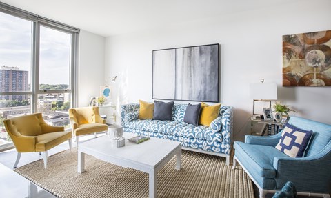 A living room with a yellow chair, a blue chair, and a white couch with a blue and white patterned cushion.