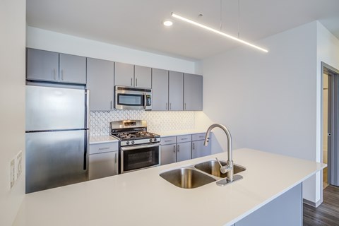 A modern kitchen with a stainless steel refrigerator, a stove with an oven, and a sink with a faucet.