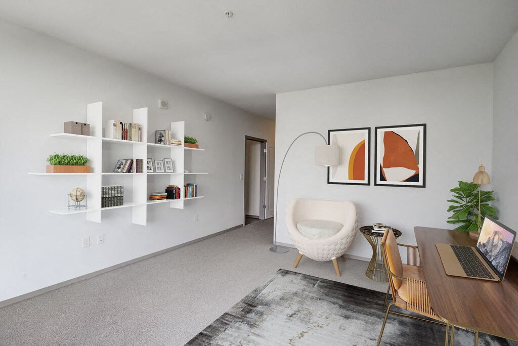 a living room with white walls and a white chair and wooden table with a laptop on it