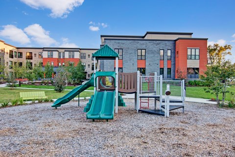 A playground with a green slide and a red and grey building in the background.