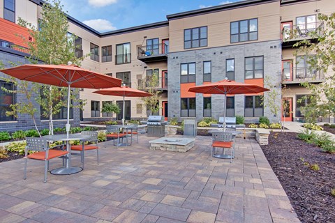A patio with tables and chairs and umbrellas in front of apartment buildings.