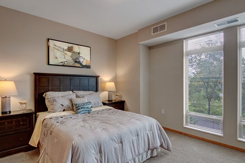 A bedroom with a large bed and a window with blinds.