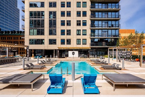 A resort-style outdoor pool here at The Nic on Fifth featuring a sleek rectangular swimming pool surrounded by modern lounge chairs, shaded pergola seating, and expansive sun decks, with a contemporary high-rise backdrop, private balconies, and an inviting courtyard layout designed for relaxing, socializing, and enjoying city views.