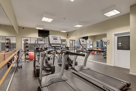 A well-equipped fitness center here at Town Centre featuring multiple treadmills, mirrored walls, free weights, and exercise balls on durable flooring, complemented by bright overhead lighting and ample space that supports cardio routines, strength training, and everyday wellness activities in a clean, organized environment.