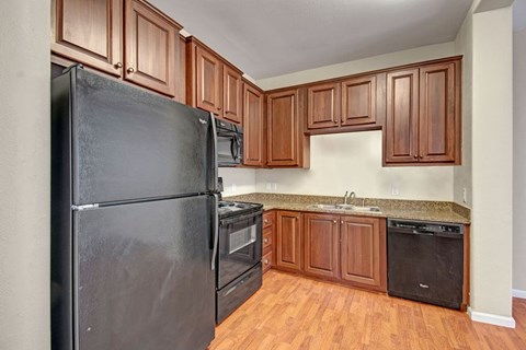 A bright kitchen here at Prairie Vista showcasing rich wood cabinetry, black appliances, granite-style countertops, wood-look flooring, and a functional L-shaped layout that offers ample storage and counter space for everyday cooking and entertaining.