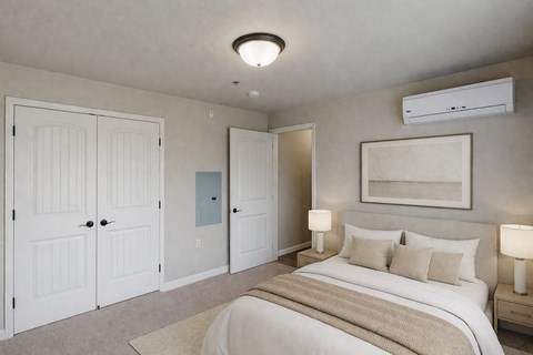 A bright, neutral bedroom here at Renaissance Heights featuring a comfortable bed with white bedding and beige accent pillows, matching bedside tables with lamps, soft carpet flooring, white double closet doors, and a wall-mounted air conditioning unit that creates a calm and inviting sleeping space.