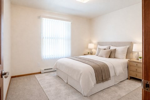 A bedroom with a large bed and a window with blinds.