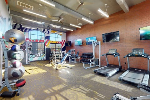 A gym with treadmills, exercise equipment, and a brick wall.