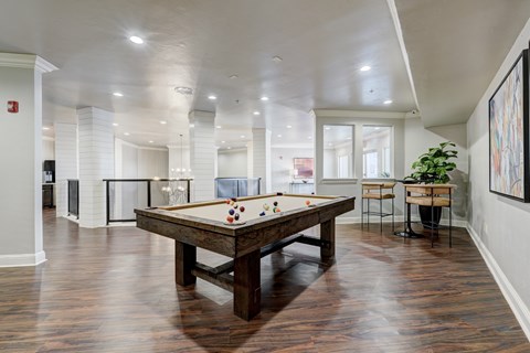A spacious game room here at Aviare Arts District with a classic pool table, wood-style flooring, modern lighting, and bar-height seating, creating a bright and inviting space for residents to relax and socialize.