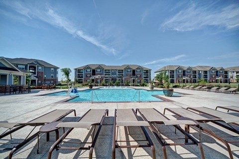 A swimming pool surrounded by sun loungers in front of apartment buildings.