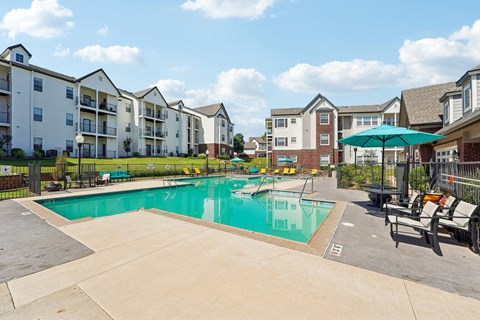 A swimming pool surrounded by apartment buildings and lounge chairs.