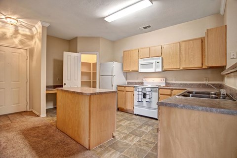 A kitchen here at Memorial Creek with light wood cabinets, a center island, neutral countertops, white appliances, tiled flooring, and an open layout connecting to the dining and living areas.A kitchen here at Memorial Creek with light wood cabinets, a center island, neutral countertops, white appliances, tiled flooring, and an open layout connecting to the dining and living areas.