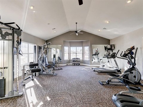 A spacious gym with a variety of equipment and a fan on the ceiling.