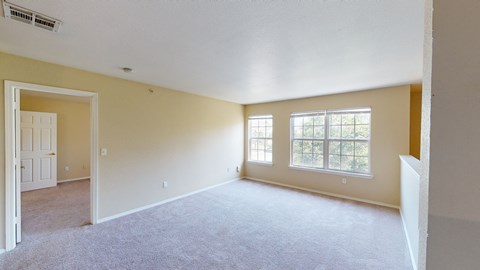 A spacious room with a carpeted floor and two windows.