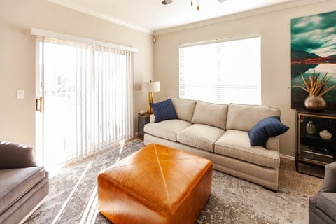 A living room with a grey couch, a brown ottoman, and a painting on the wall.