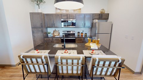 A kitchen with a table set for two with a sink and refrigerator in the background.