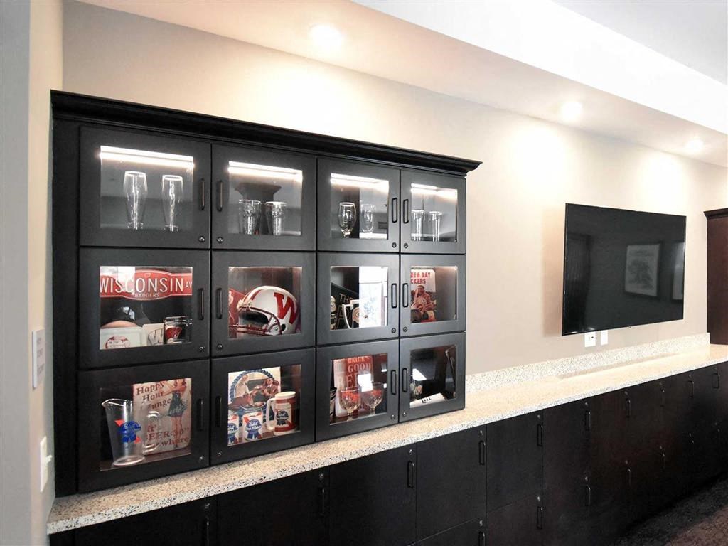 Black display cabinet with sports memorabilia and glasses at the Oaks of Shorewood Apartments, set against a light wall next to a large flat-screen TV. Modern and organized ambiance.