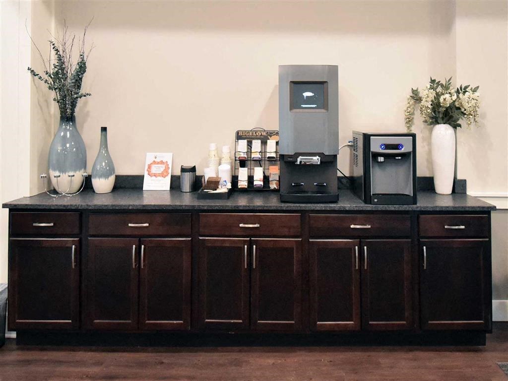 Coffee station with a modern coffee machine and water dispenser on a dark wooden cabinet at the Oaks of Shorewood Apartments. Decorated with tall vases and flowers, creating a welcoming atmosphere.
