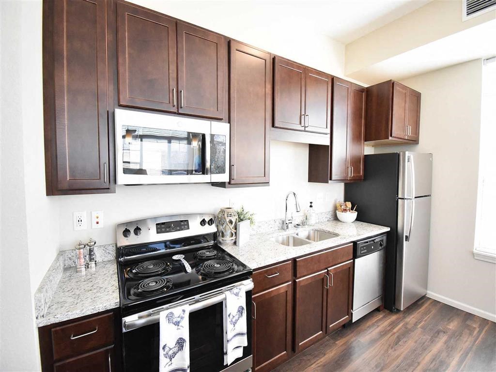 Modern kitchen with dark wooden cabinets, stainless steel appliances, and a granite countertop. Bright and clean with a cozy, inviting feel. The Oaks of Shorewood Apartments.