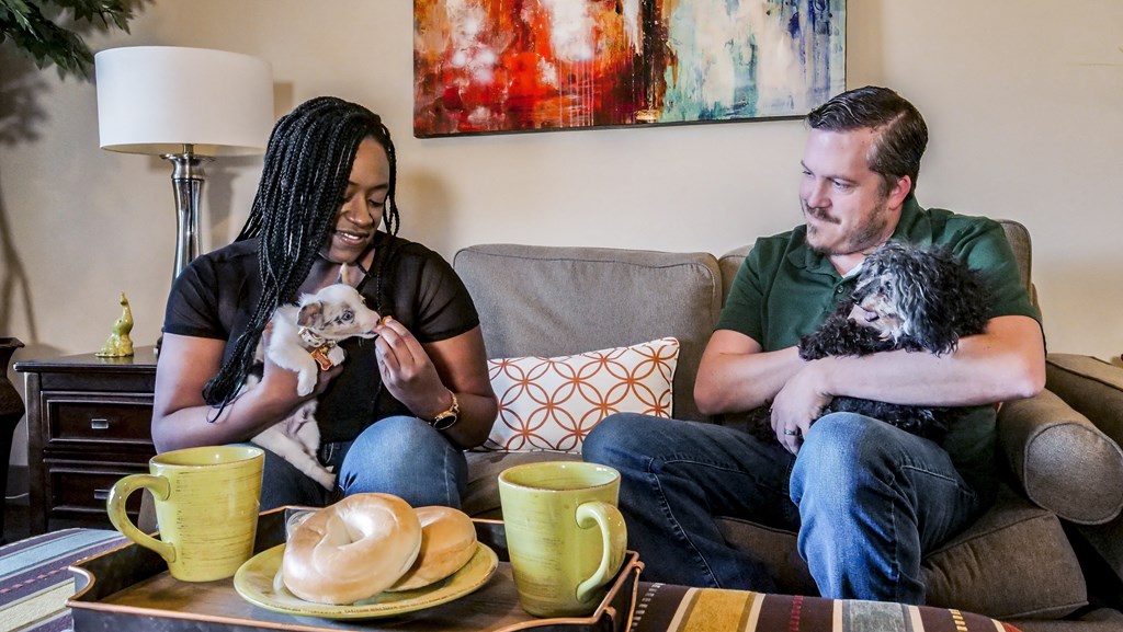 A man and woman sitting on a couch with two dogs at Confluence at Harvest Hills