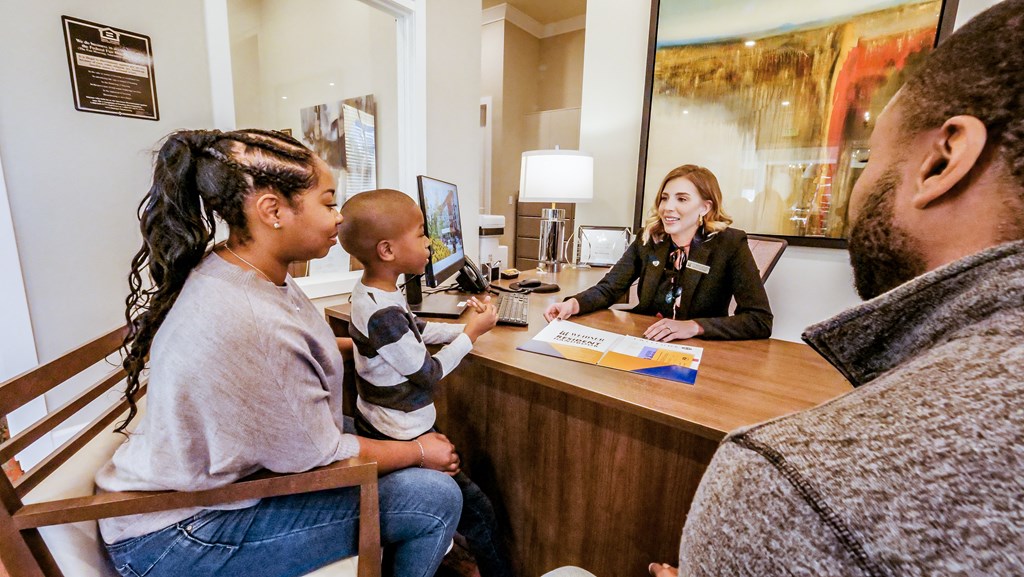 A woman sitting at a desk talking to a family at a reception desk at Confluence at Harvest  Hills.