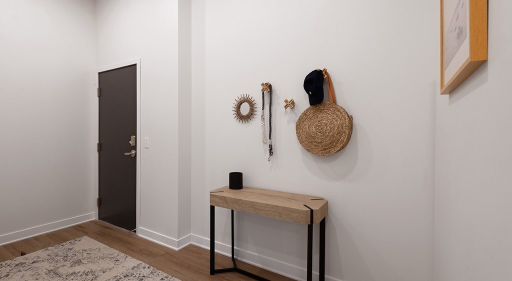 A room with a black door, a table with a speaker on it, and a basket on the wall.