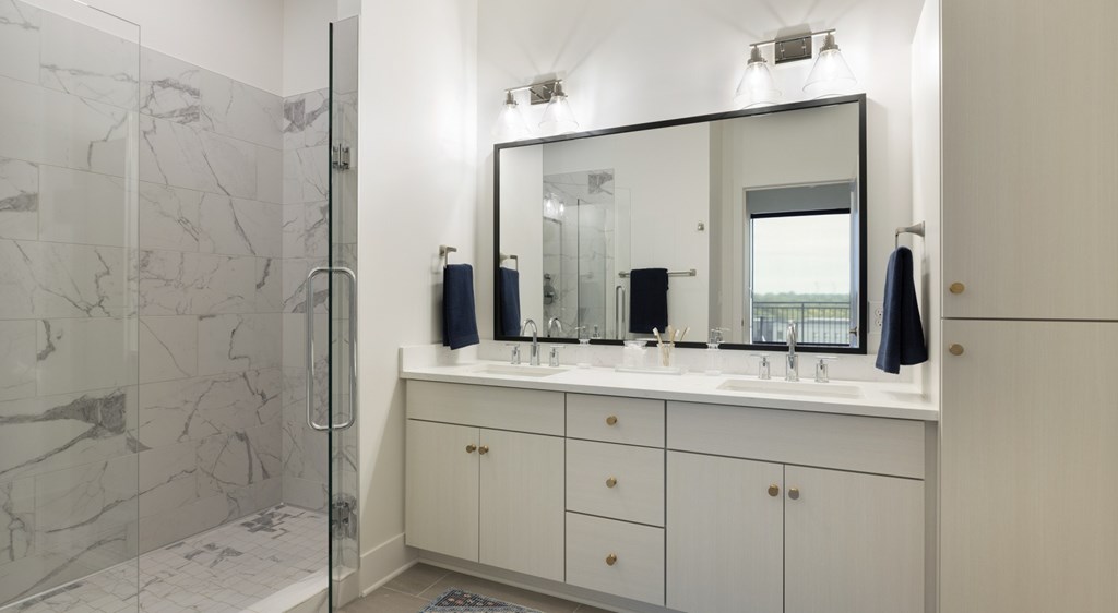 A bathroom with a marble shower, white vanity, and a large mirror.