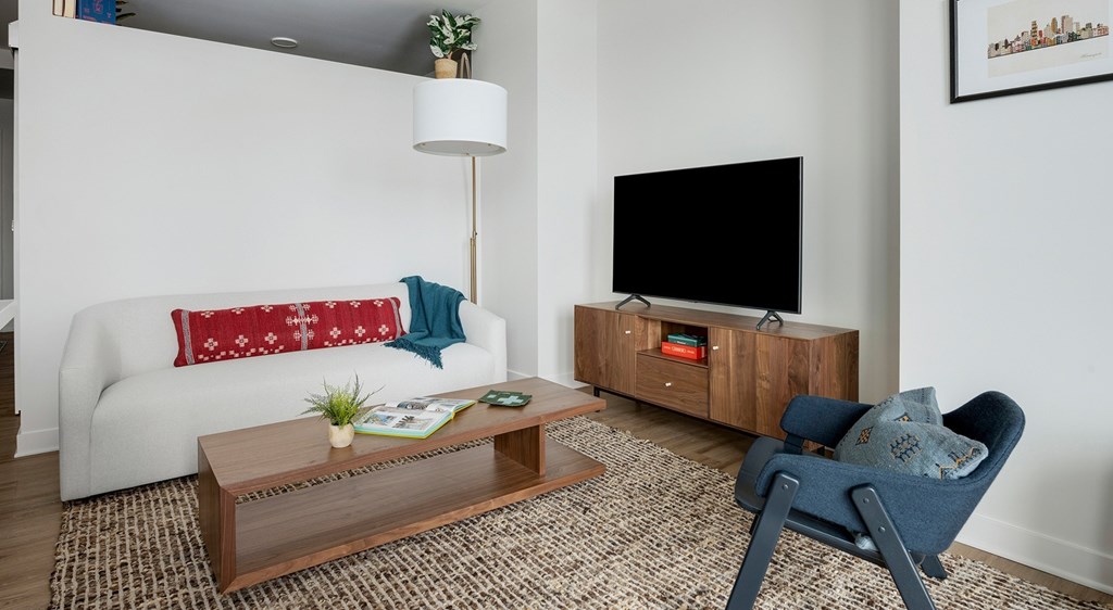 A living room with a white sofa, a wooden coffee table, a blue chair, and a flat screen TV.