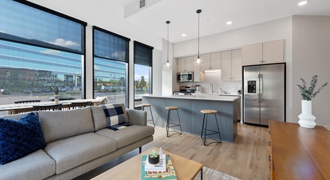 A modern living room with a grey sofa and a kitchen area in the background.