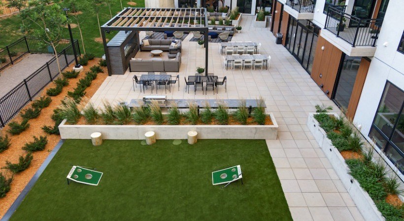 A patio with a table and chairs is surrounded by a green lawn.
