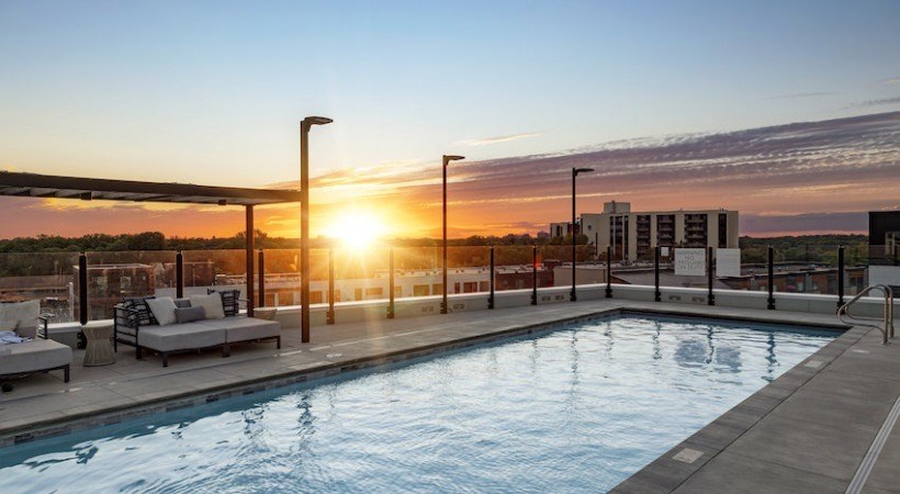 A sunset view of a pool area with lounge chairs and a building in the background.