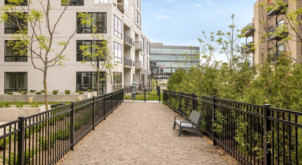 A black fence runs along a brick pathway between two buildings.