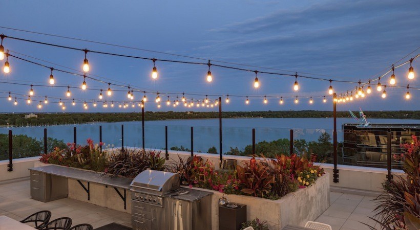 A patio with a bench and lights strung across the top.